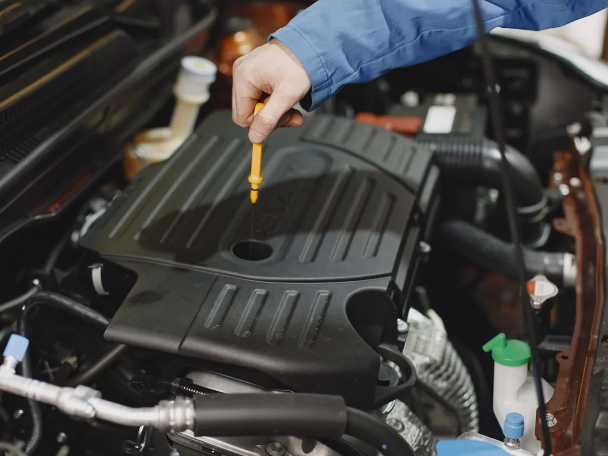 A hand checking the oil level beneath an open car hood