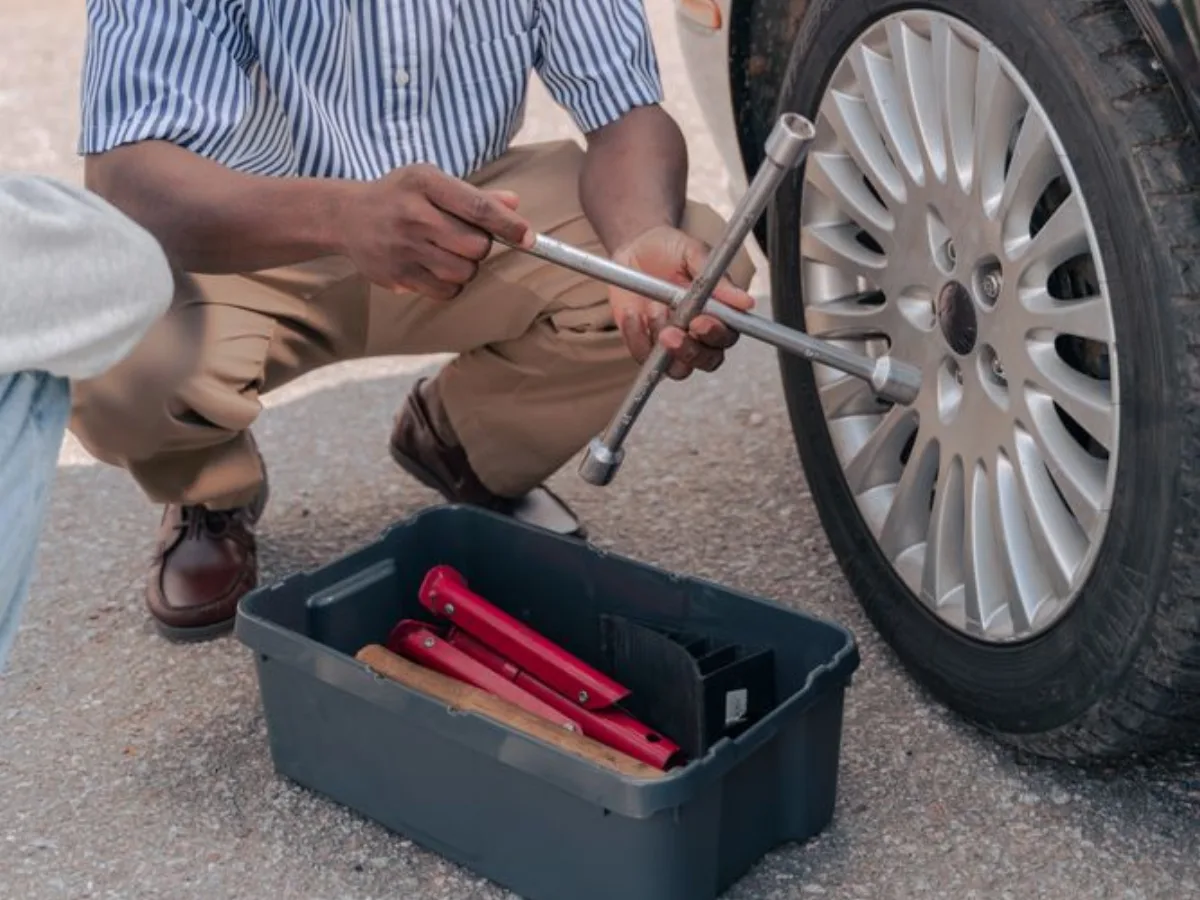Hands using a wheel wrench beside a car tire outdoors